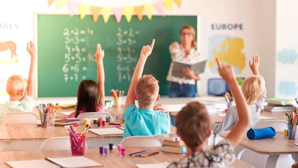 Classroom of students raising hands for teacher 