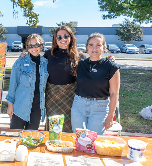 Three recent graduate Halff employees taking a photo at Halff's annual Chili Cook-Off table outside